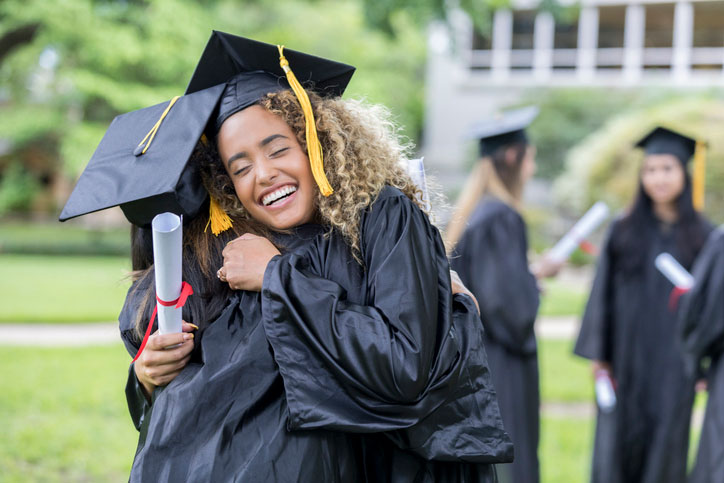 college grads hugging on graduation day